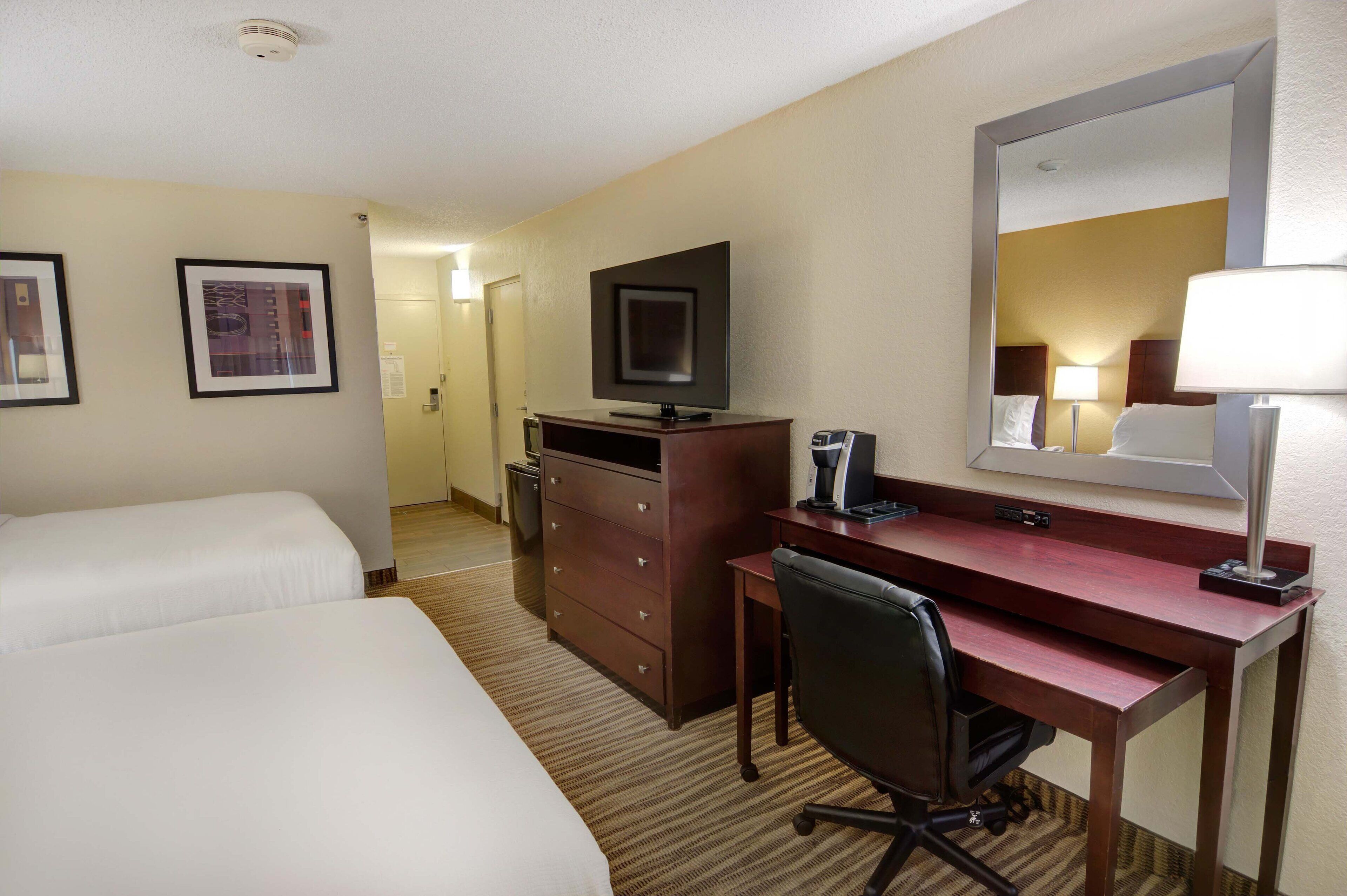 Une chambre d’hôtel avec deux lits, un bureau, une chaise, une t élévision, un miroir et une lampe.