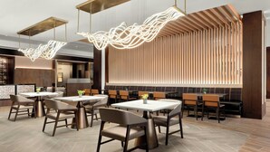 Un interior de restaurante moderno con mesas y sillas altas, iluminación colgante y una pared de listones de madera.