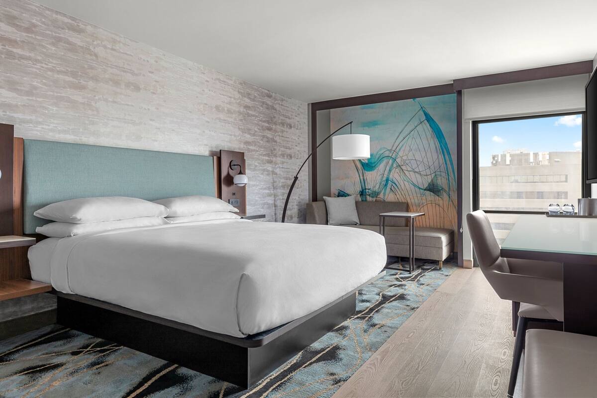 Quarto de hotel moderno com uma cama grande, uma escrivaninha e vista para a cidade.