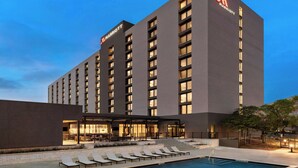 Un hotel moderno con un amplio área de piscina, mobiliario exterior y un logotipo de Marriott destacado.