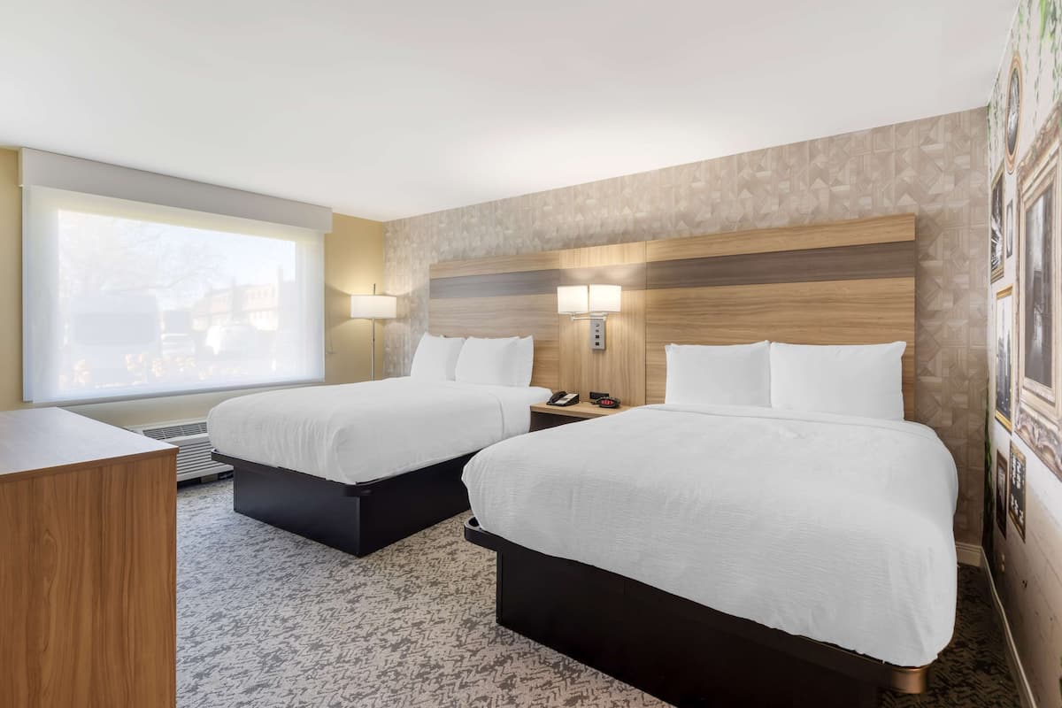 A hotel room with two beds, a desk, and a large window.