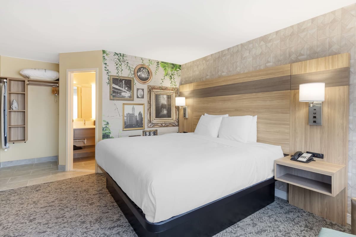 A hotel room with a large bed, a bedside table with a lamp, a wall-mounted phone, and a built-in shelf.