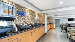 A hotel kitchen with a coffee machine, a sign for Energize Protein, and a tiled backsplash.