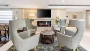 A modern living room with grey upholstered armchairs, a round coffee table, and a flat-screen TV above a fireplace.