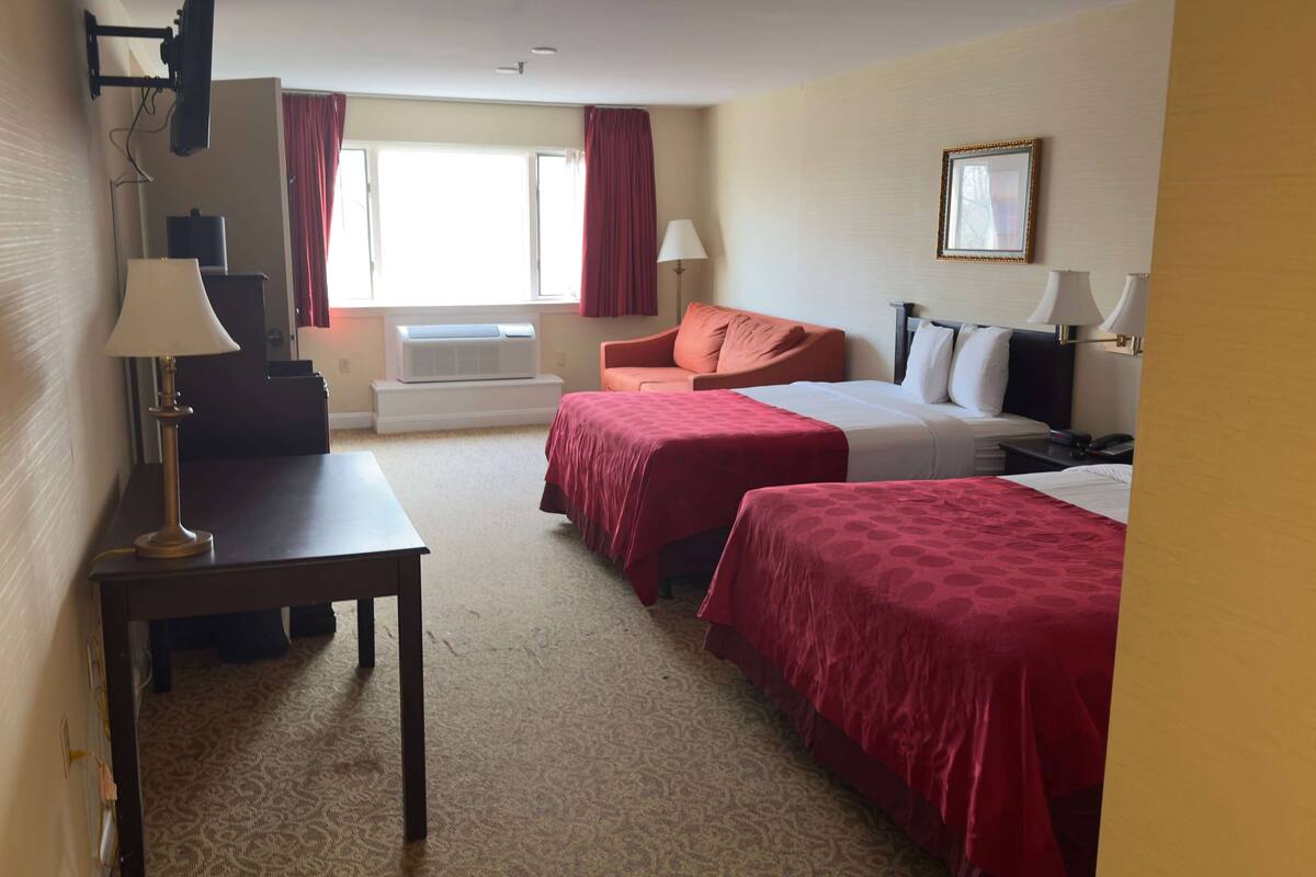 Een hotelkamer met twee bedden, een bureau, een stoel, een televisie en een raam met gordijnen.