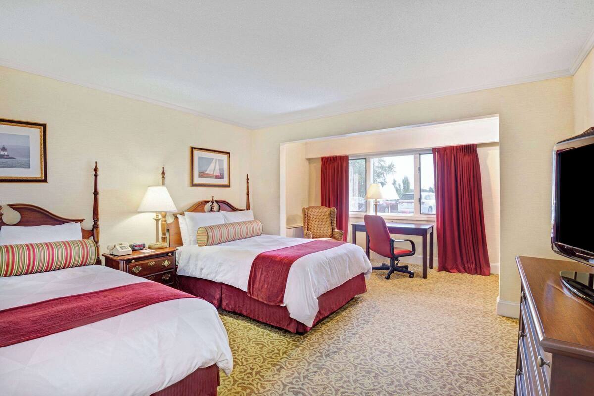 Een hotelkamer met twee bedden, een bureau, een stoel, een televisie en een raam met gordijnen.