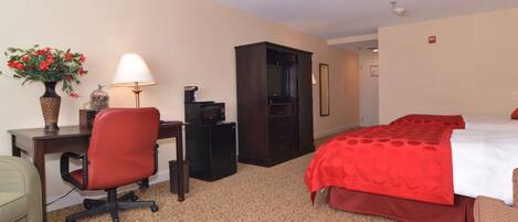 A hotel room with a bed, desk, chair, and a small cabinet.