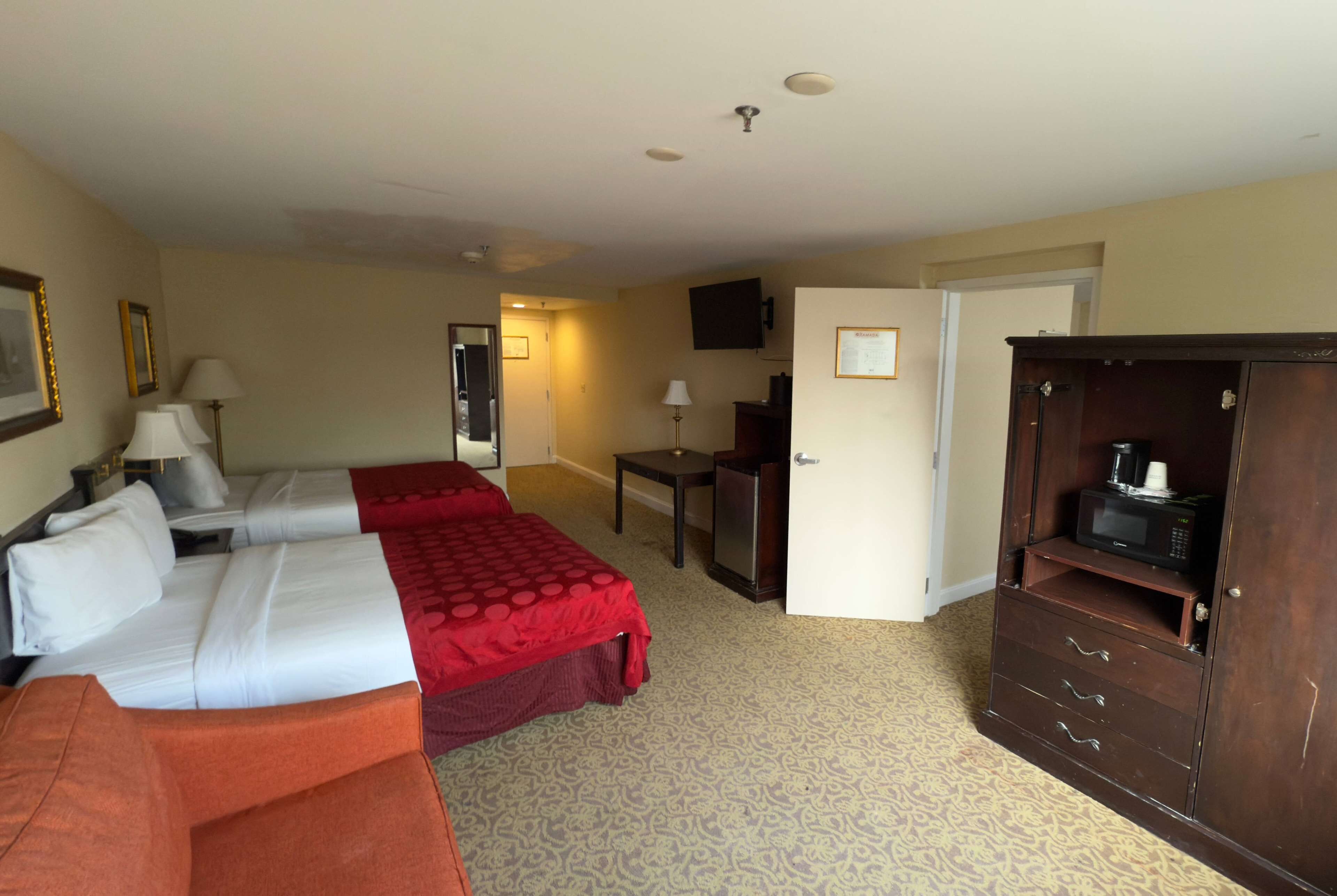 A hotel room with two beds, a sofa, a desk, a television, and a wardrobe.