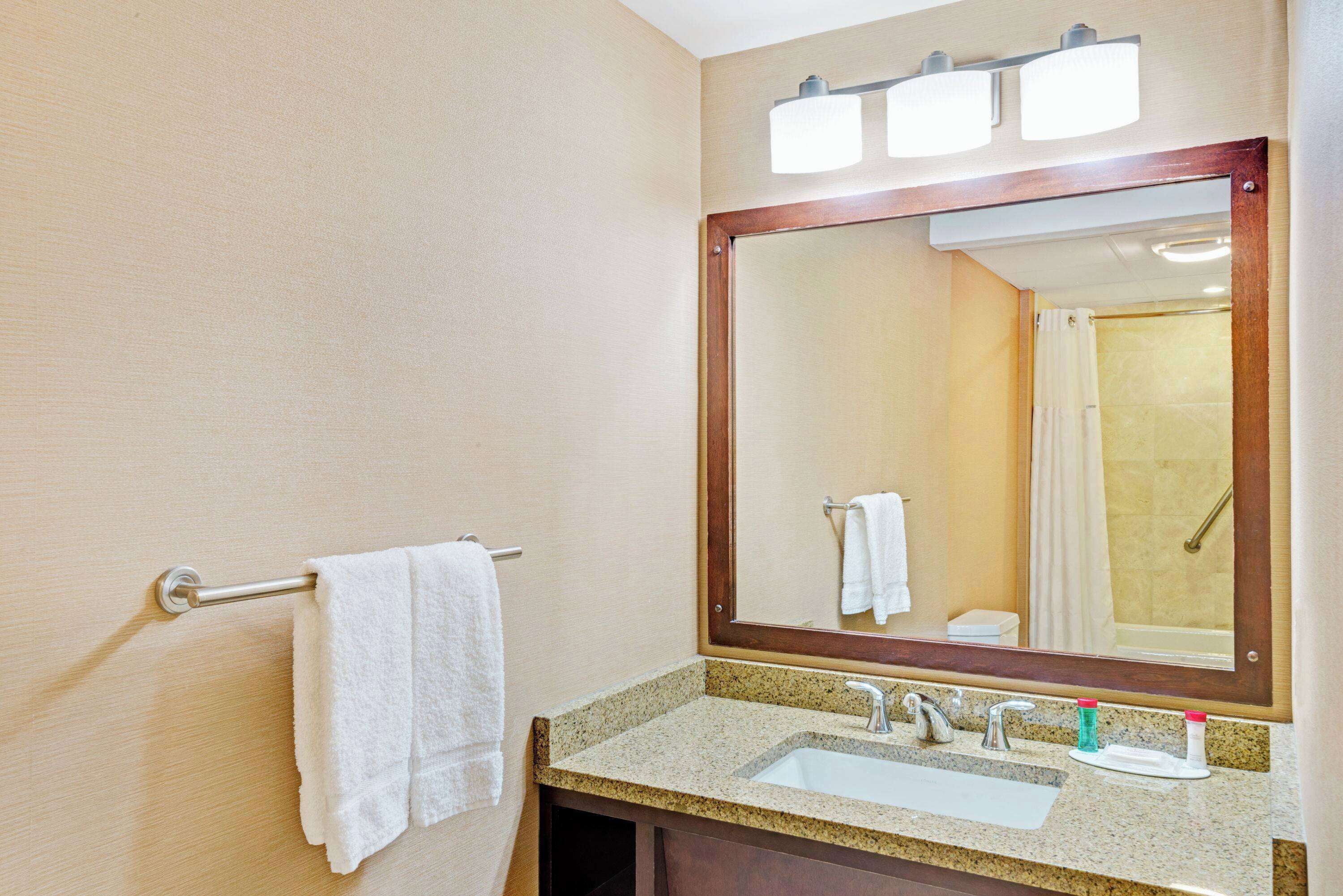 A bathroom with a sink, mirror, towel rack, and a shower visible in the reflection.