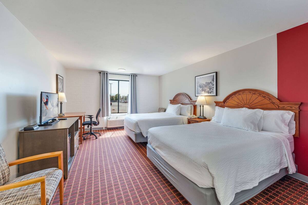 A hotel room with two beds, a desk with a computer, a chair, and a view of the city through the window.