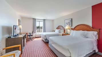 A hotel room with two beds, a desk with a computer, a chair, and a view of the city through the window.