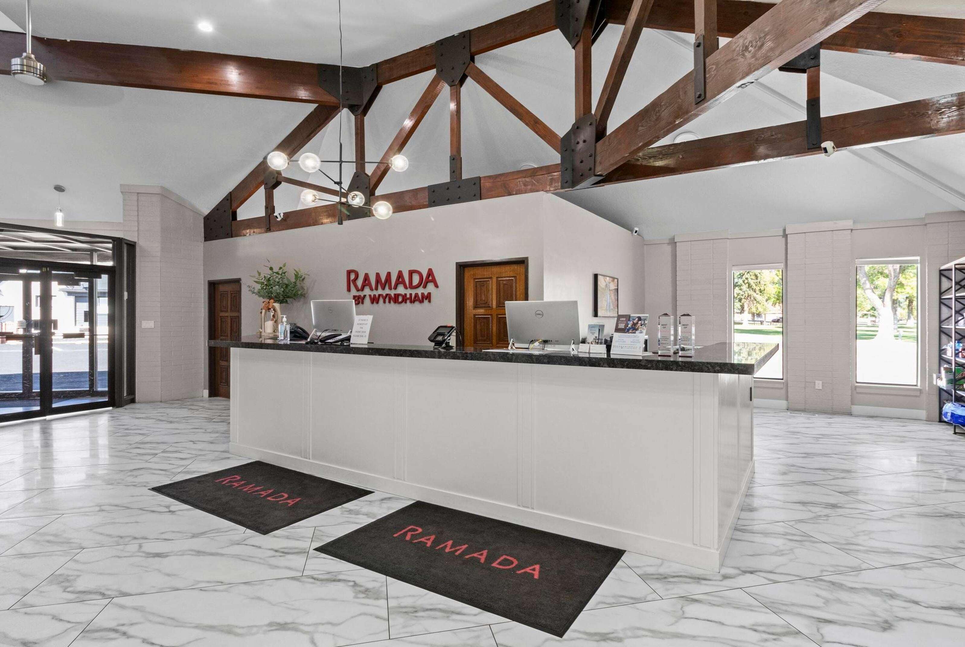 Ein Empfangsbereich mit Marmorboden, einer Rezeption und einem Schild mit der Aufschrift 'RAMADA BY WYNDHAM'.