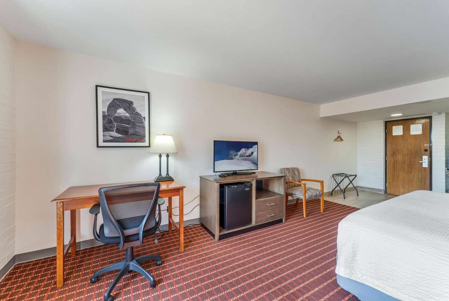 Habitación de hotel con cama, escritorio, silla, televisor y refrigerador pequeño.