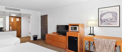 A hotel room with a bed, a desk with a lamp, a television, a microwave, and a small refrigerator.