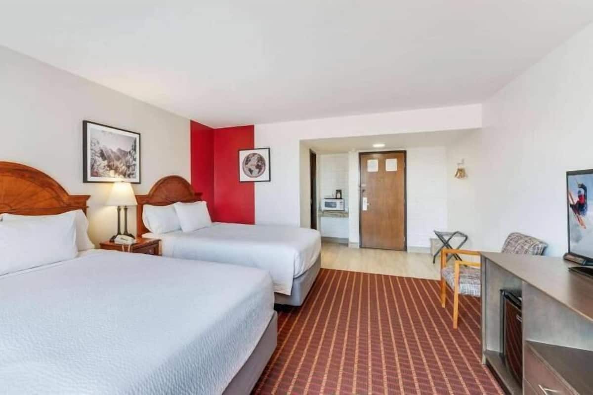 A hotel room with two beds, a desk, a chair, and a television.