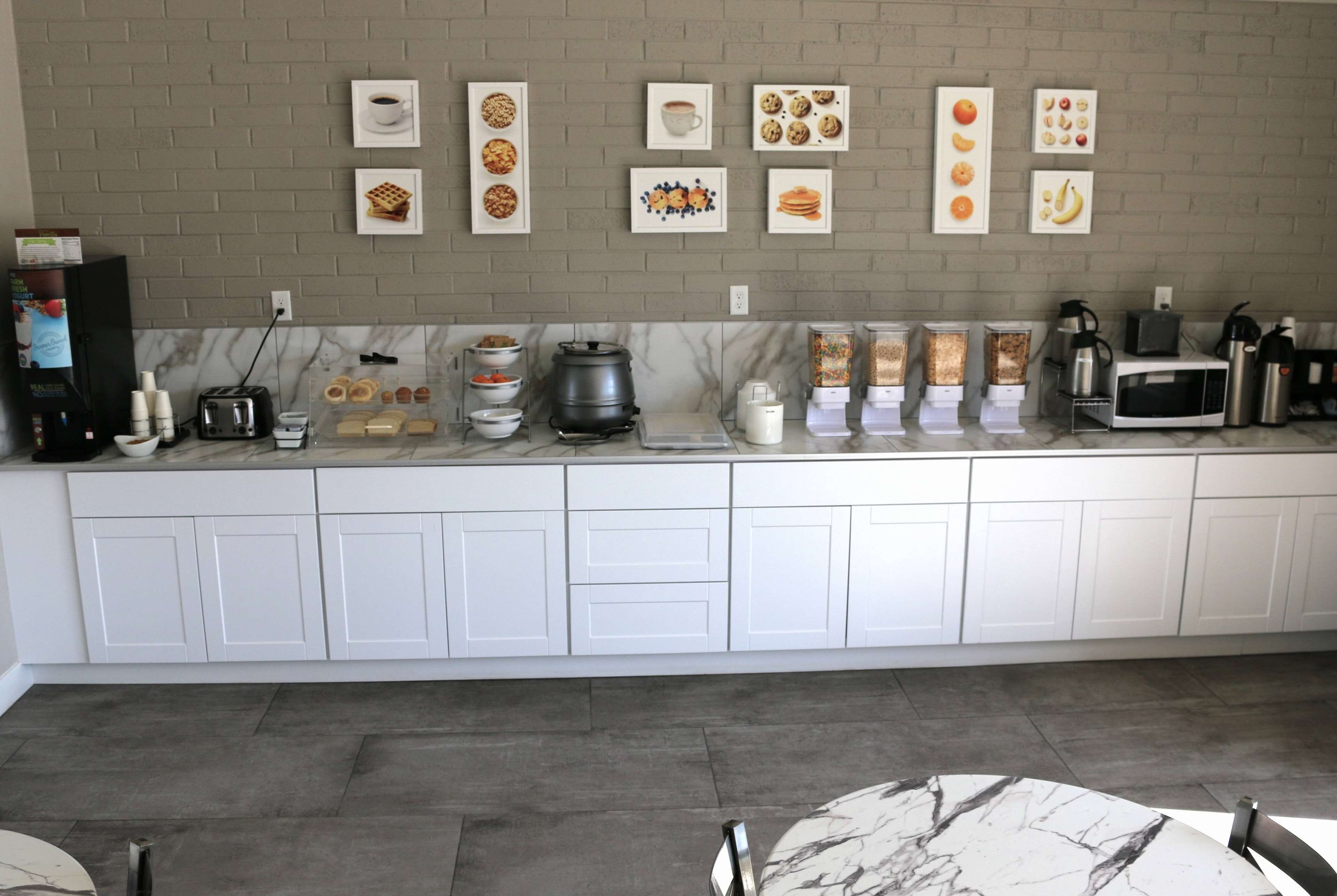 A modern kitchen with white cabinets, a marble countertop, and various appliances including a coffee maker, toaster, and microwave.