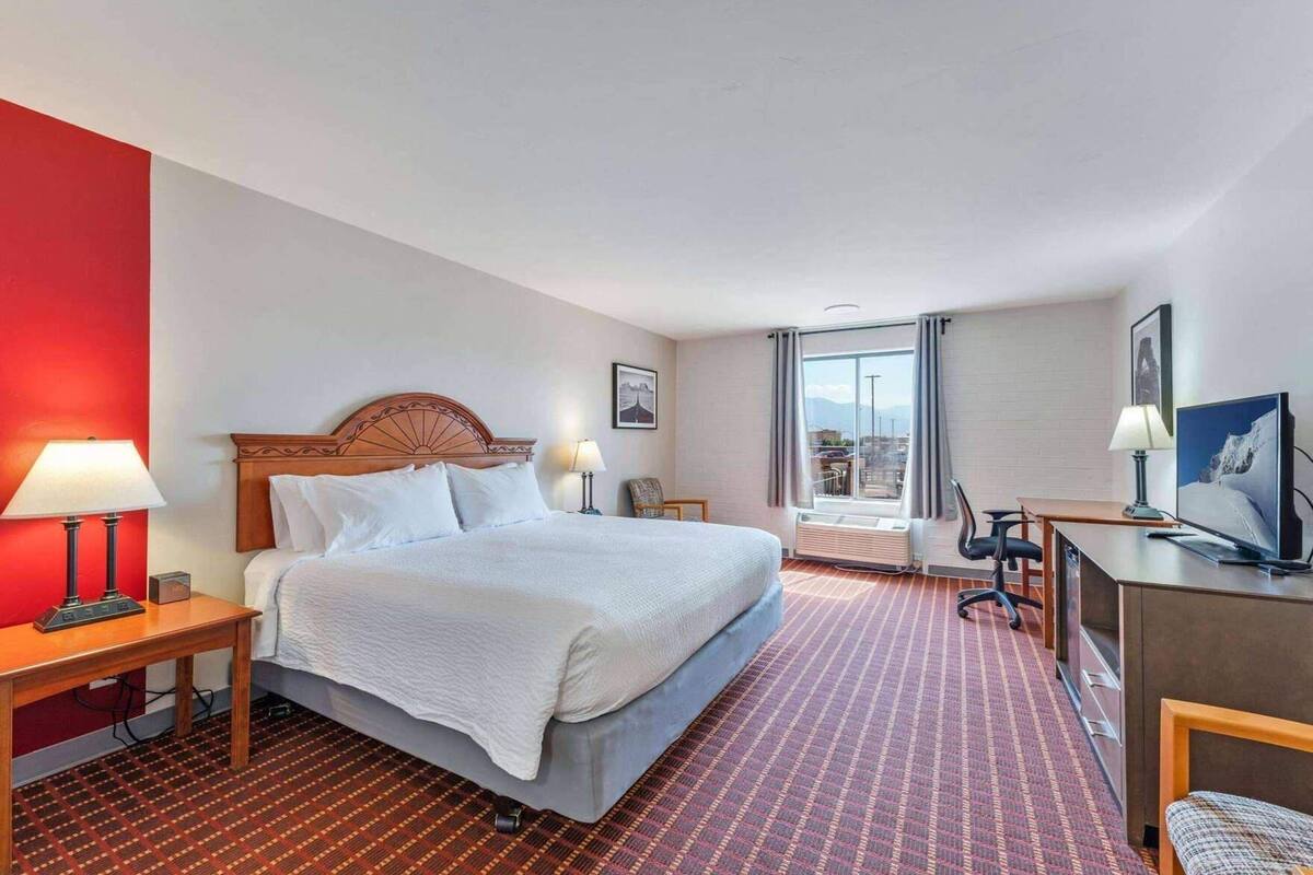 A hotel room with a bed, bedside tables, a desk, a chair, a TV, and a window with a view.
