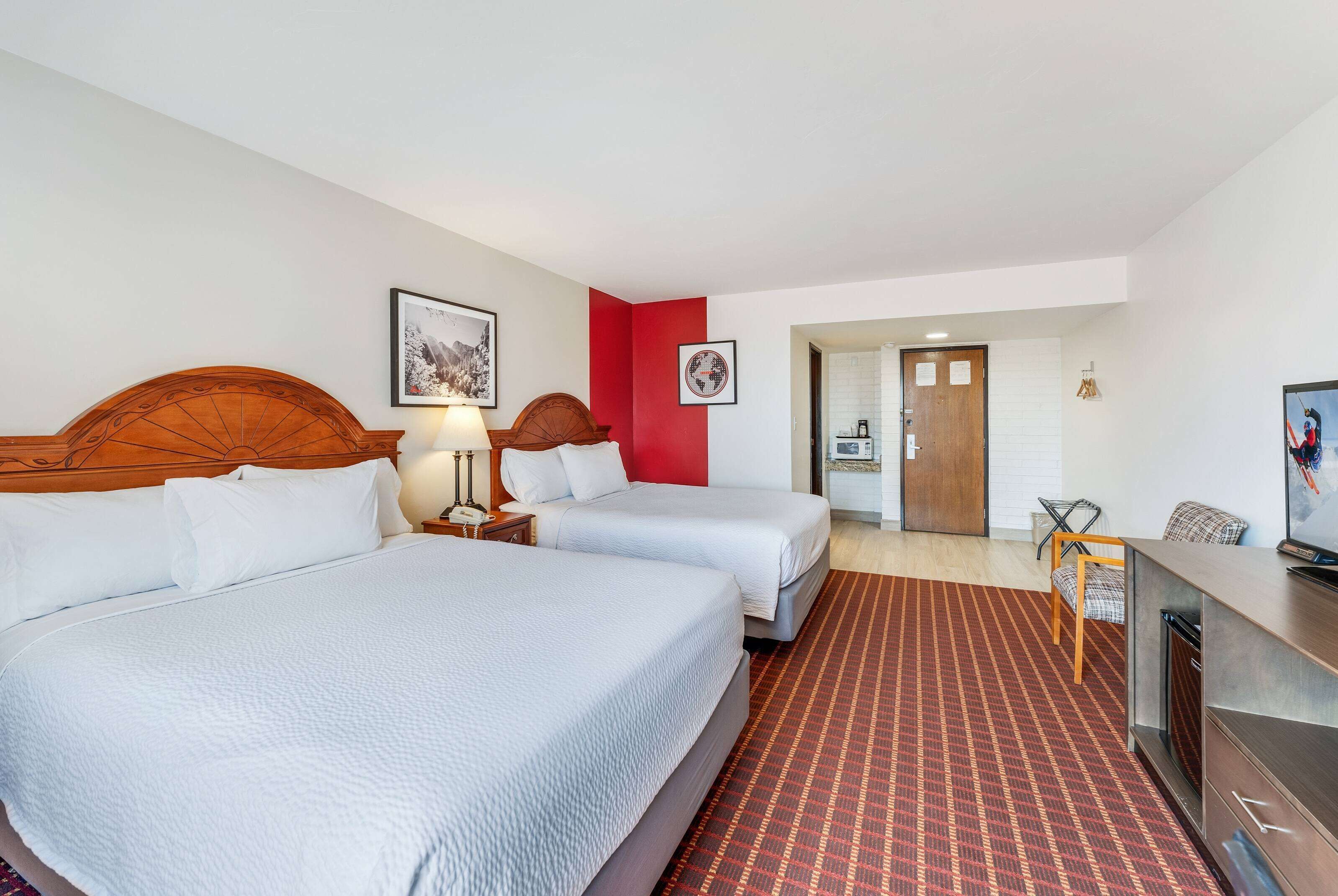 Habitación de hotel con dos camas, un escritorio, una silla y un televisor.