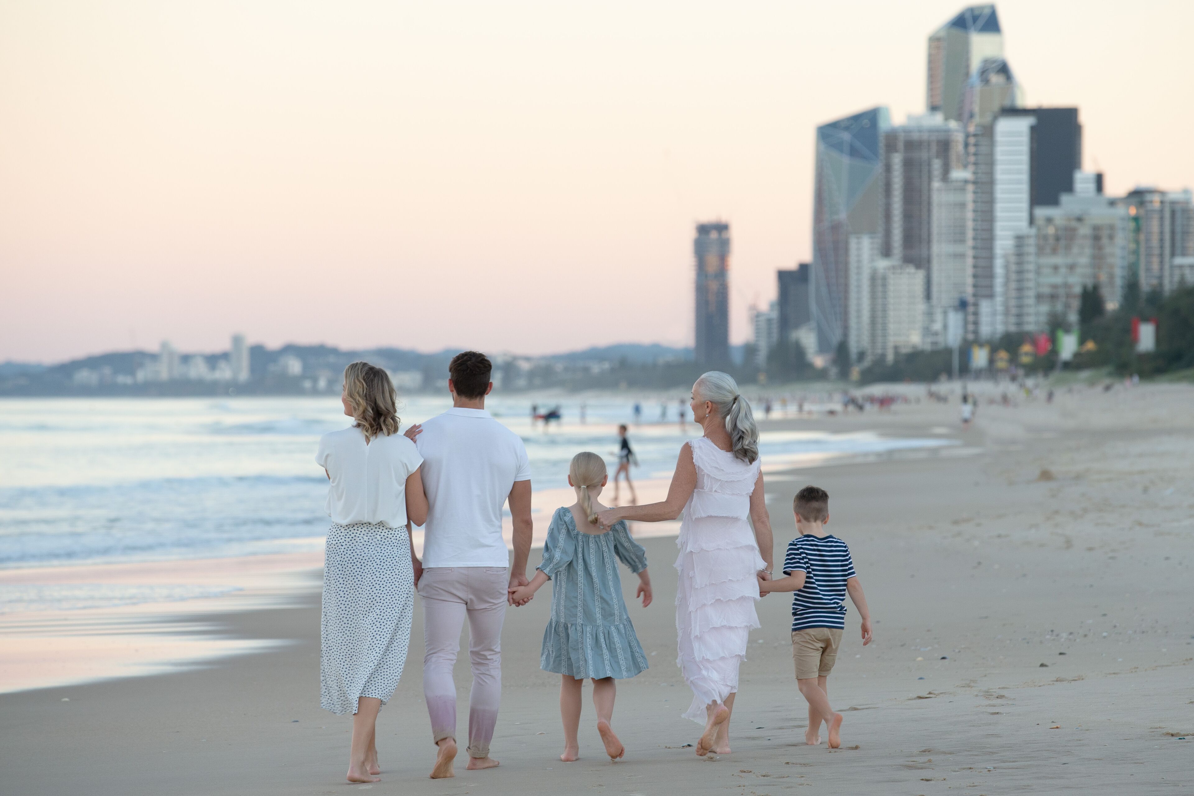 A family walking on a beach with a city skyline in the background.