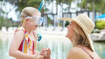 A person in a straw hat and striped swimsuit holding hands with a child wearing a snorkel mask and a striped swimsuit.