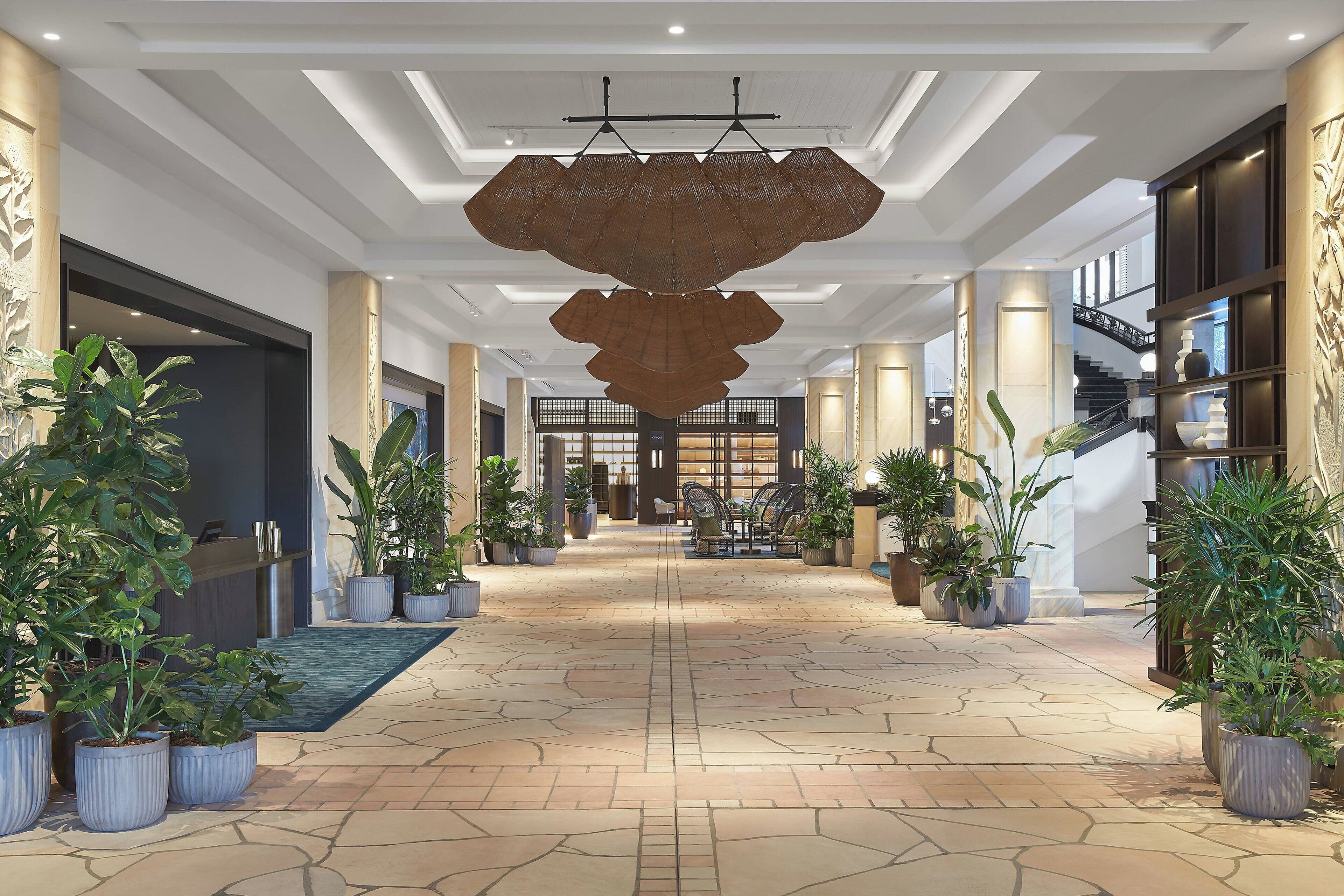 Un hall d’entrée spacieux avec un espace salon central, des plantes en pot et un escalier en arrière-plan.