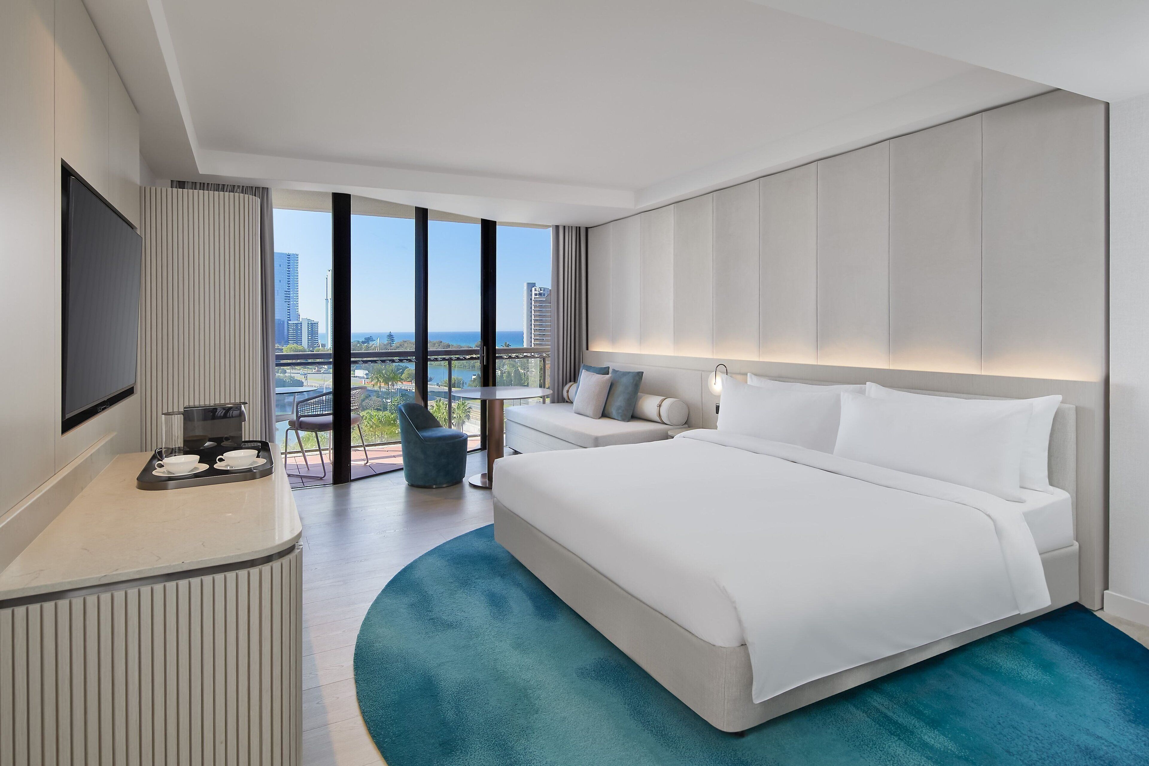 Una habitación de hotel moderna con una cama grande, un área de estar con un sofá y sillones, una estación de café y un amplio ventanal con vistas a la ciudad.