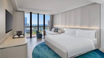 Una habitación de hotel moderna con una cama grande, un área de estar con un sofá y sillones, una estación de café y un amplio ventanal con vistas a la ciudad.