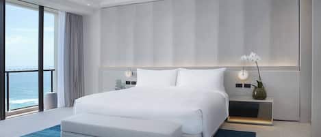 Une chambre d’hôtel moderne avec un grand lit, une table de chevet avec une lampe, un vase de fleurs et une vue sur l’océan.