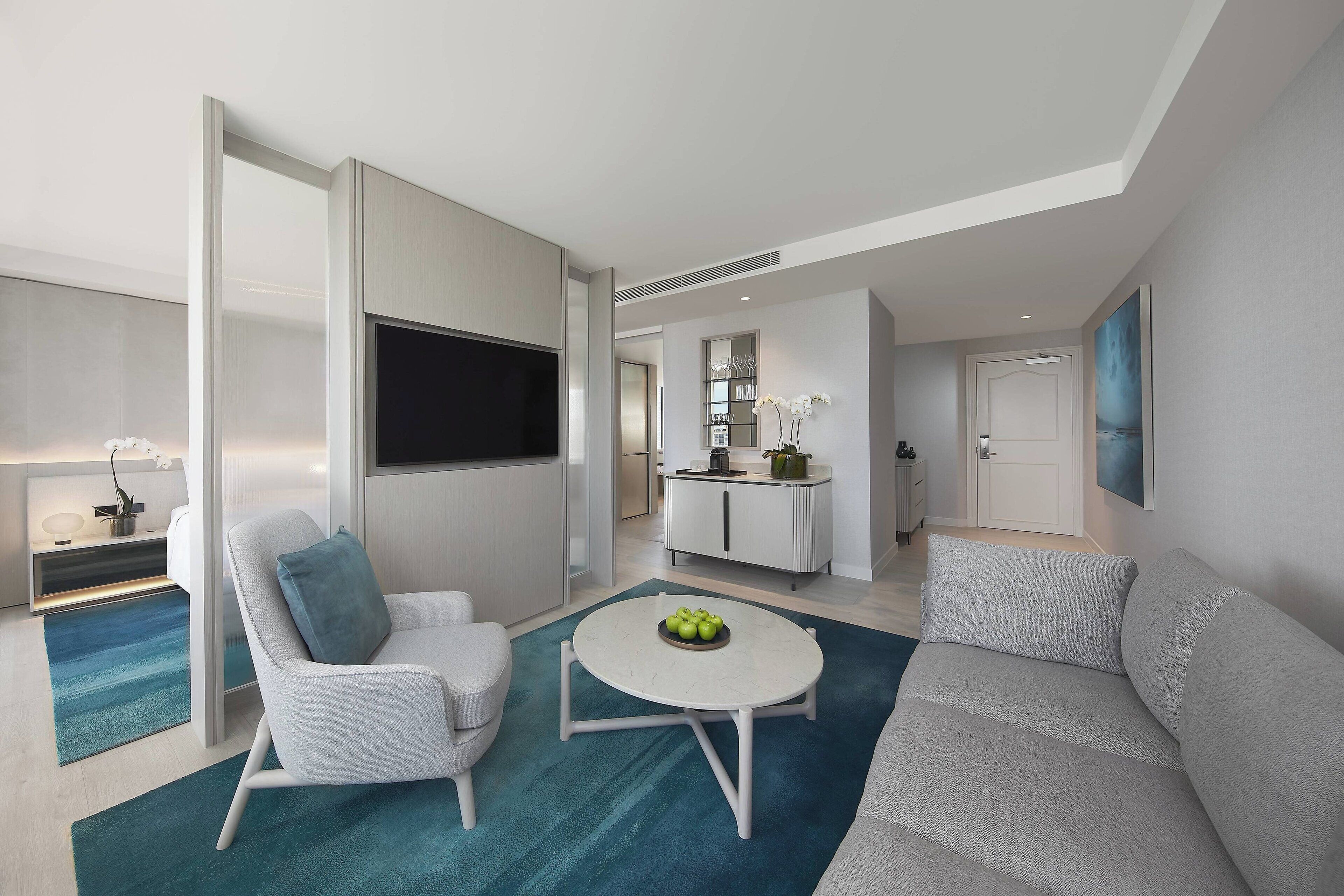 A modern living room with a sofa, a chair, a coffee table, and a TV. There is a kitchen area in the background.
