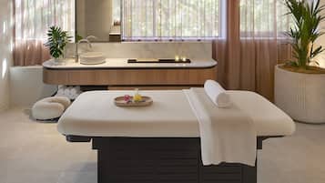 Relax in this serene spa room featuring a central massage table, a vanity with sink, and a large mirror.