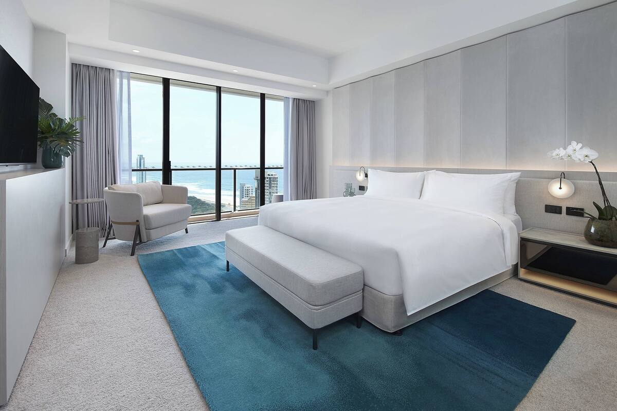 A modern hotel room with a large bed, a seating area, and a view of the city.