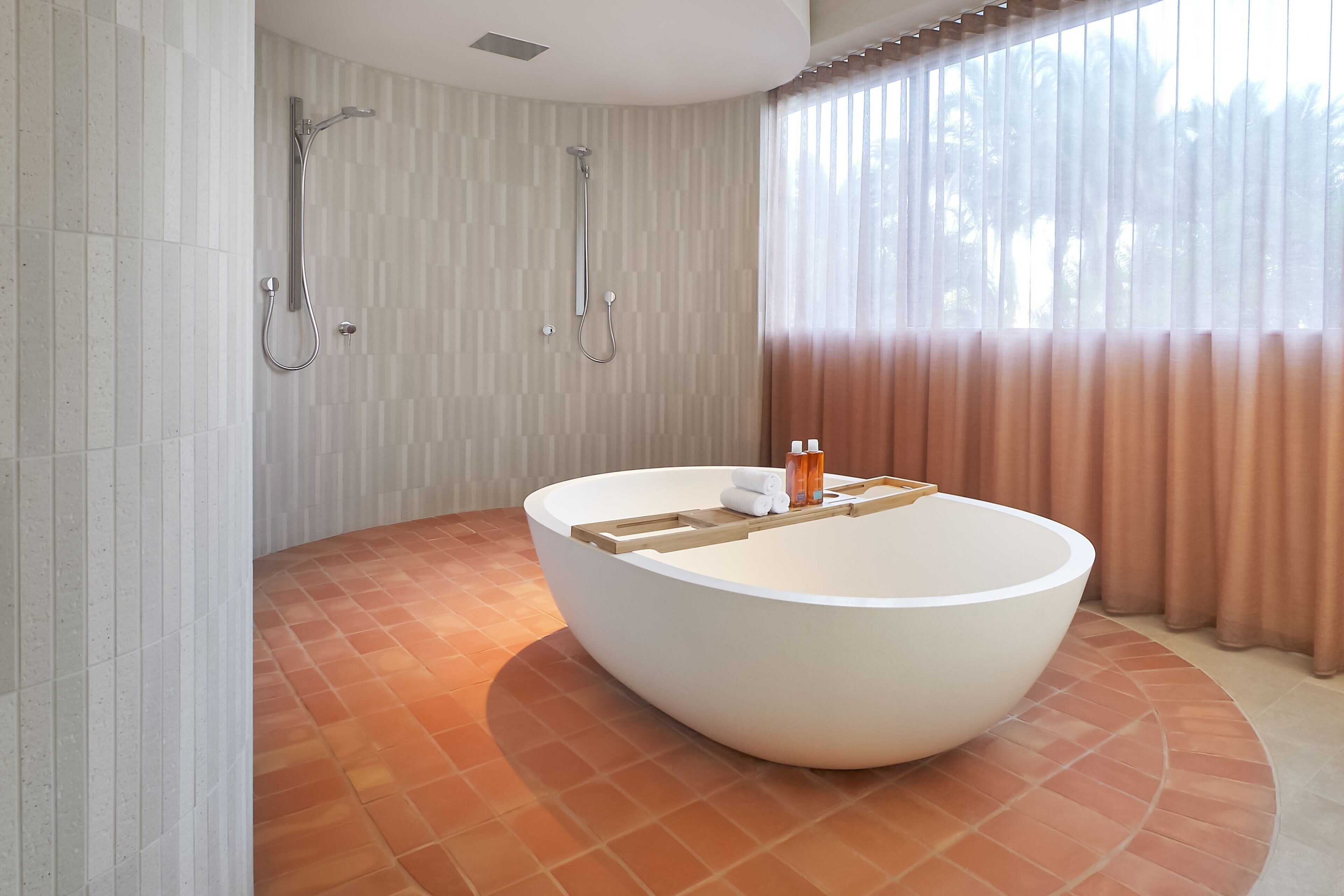 A modern bathroom with a large freestanding bathtub, a showerhead, and a window with curtains.