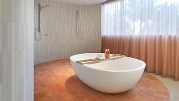 A modern bathroom with a large freestanding bathtub, a showerhead, and a window with curtains.