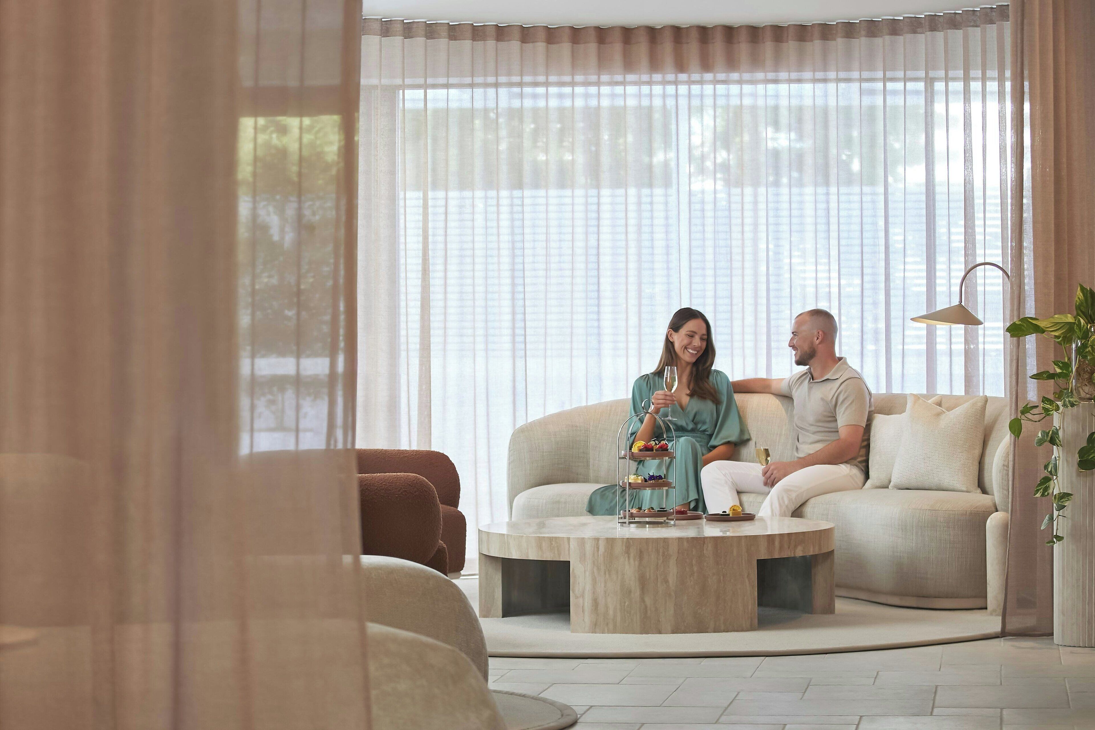 Ein modernes Wohnzimmer mit einem beigen Sofa, einem runden Couchtisch und transparenten Vorhängen.