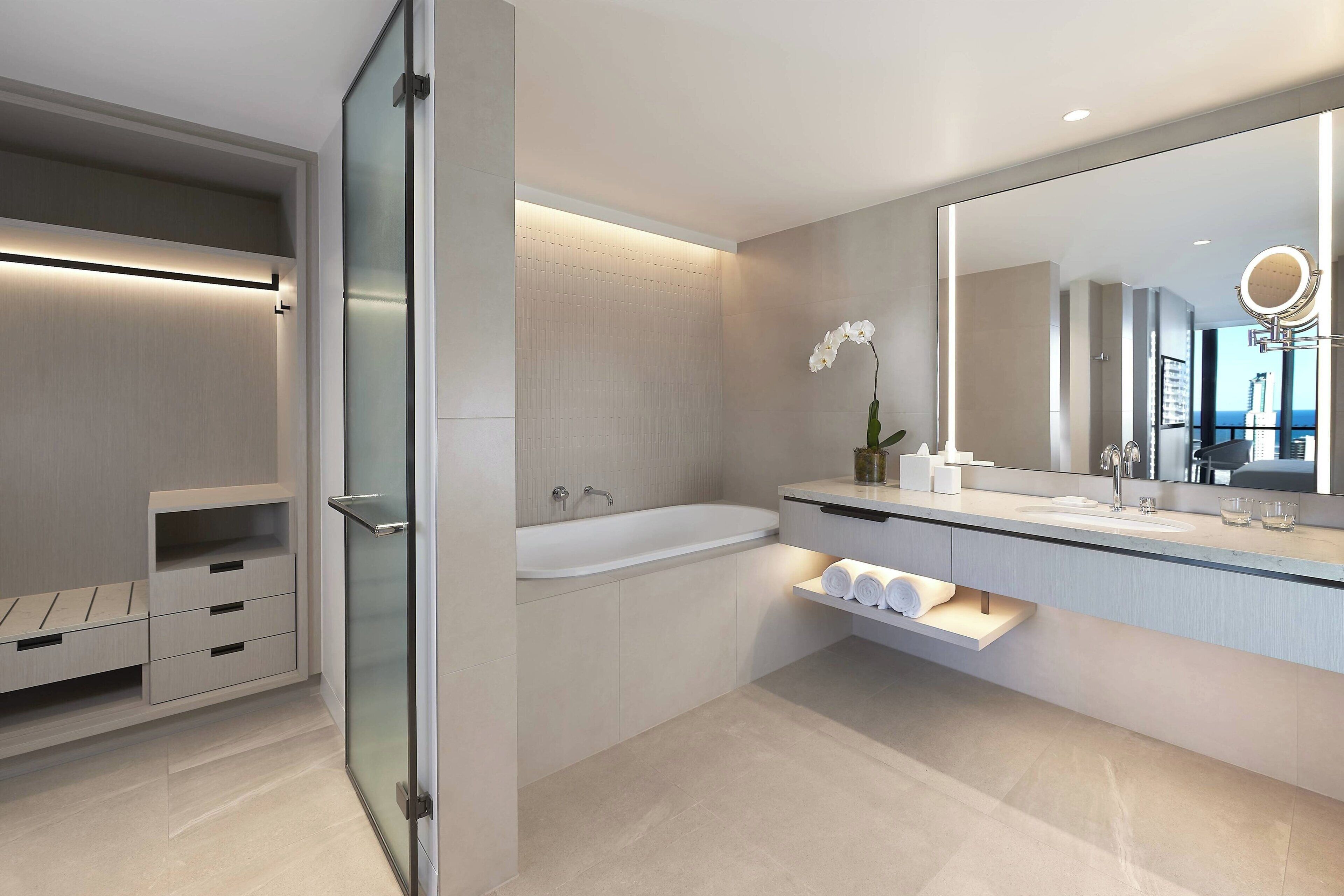 A modern bathroom with a glass shower enclosure, a freestanding bathtub, and a large mirror with a round light.