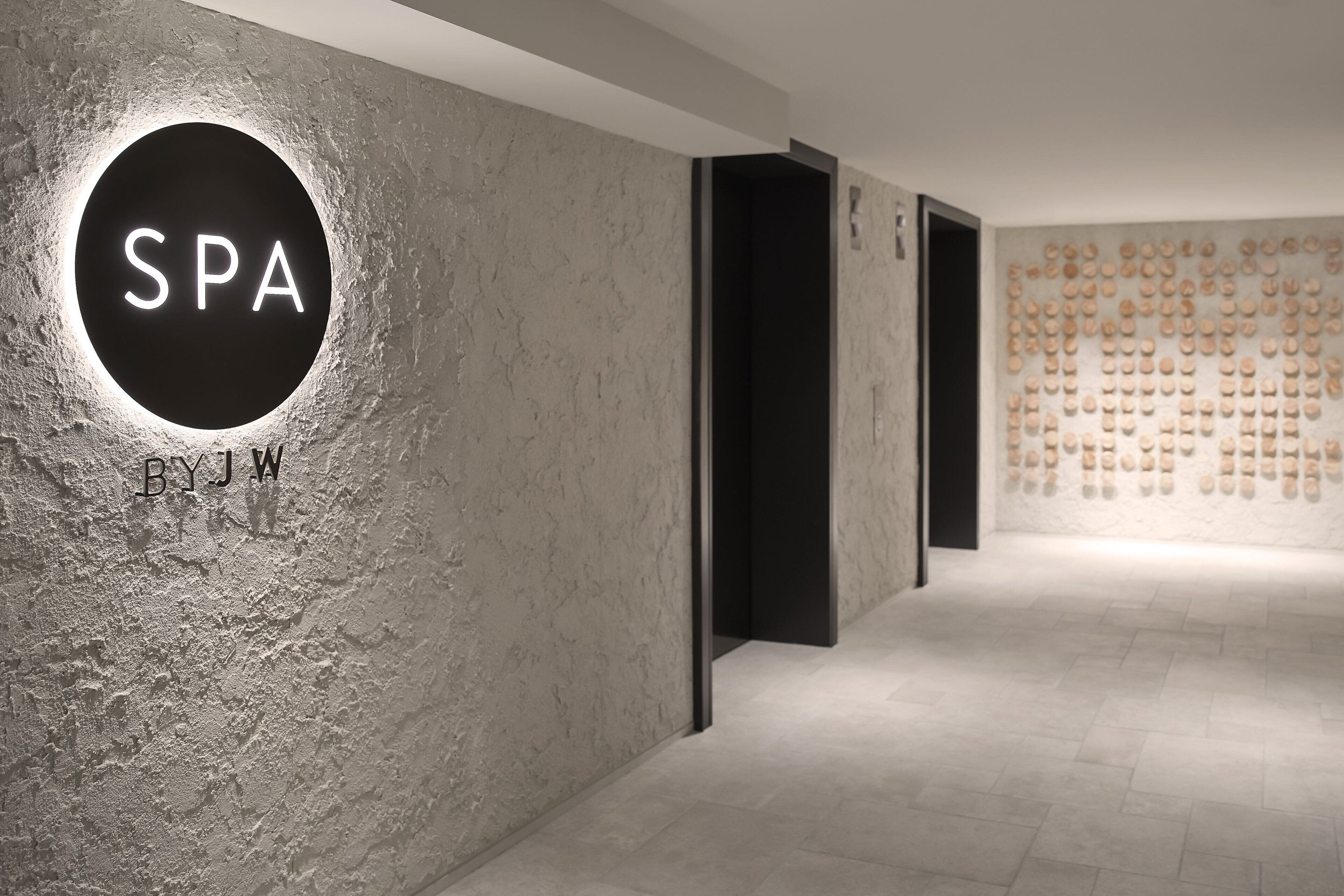 Uma área de spa com uma placa circular com a inscrição "SPA BYJW" e uma parede com vários pequenos frascos.