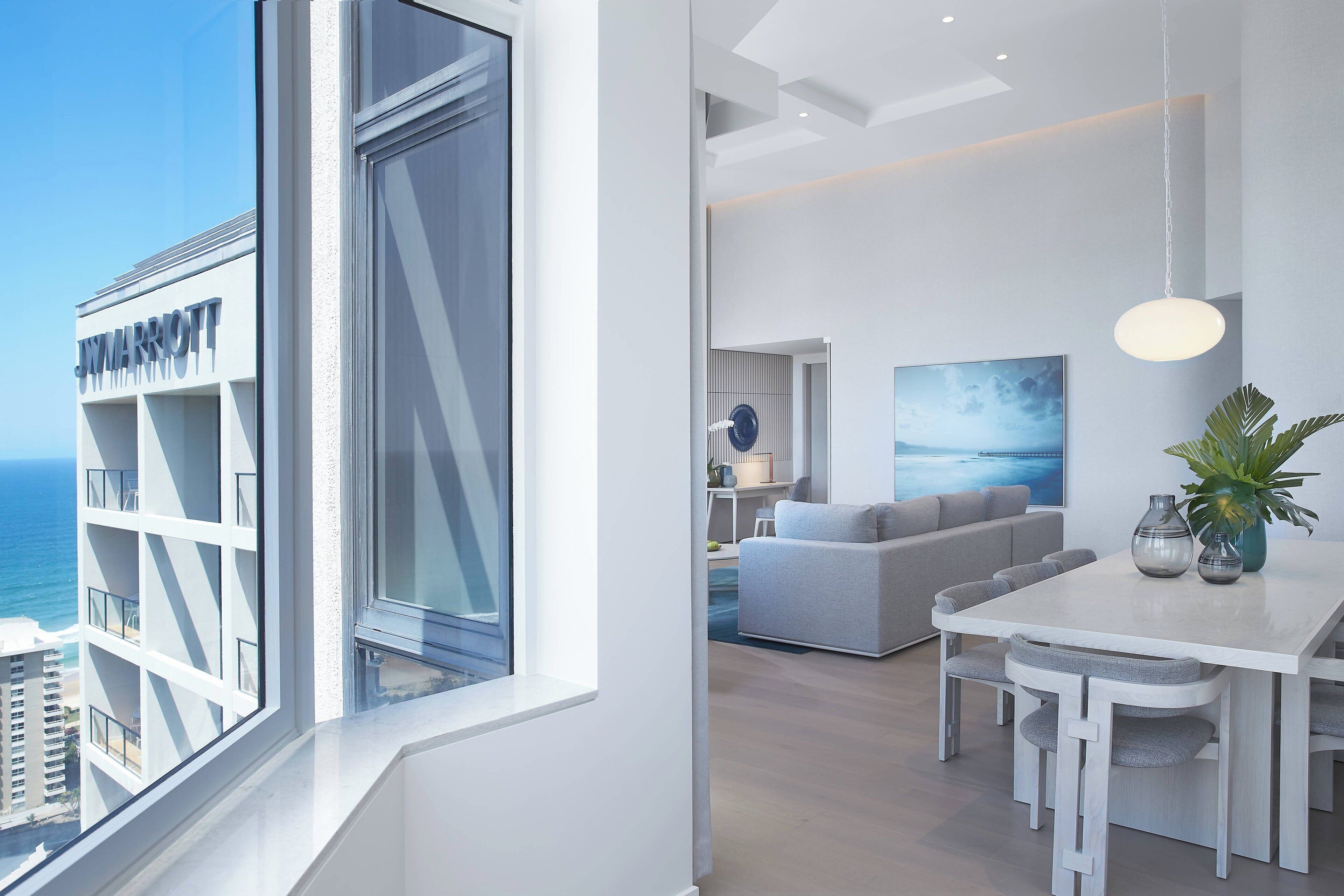 A modern hotel room with a large window, a dining area, and a living space.