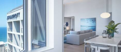 A modern hotel room with a large window, a dining area, and a living space.