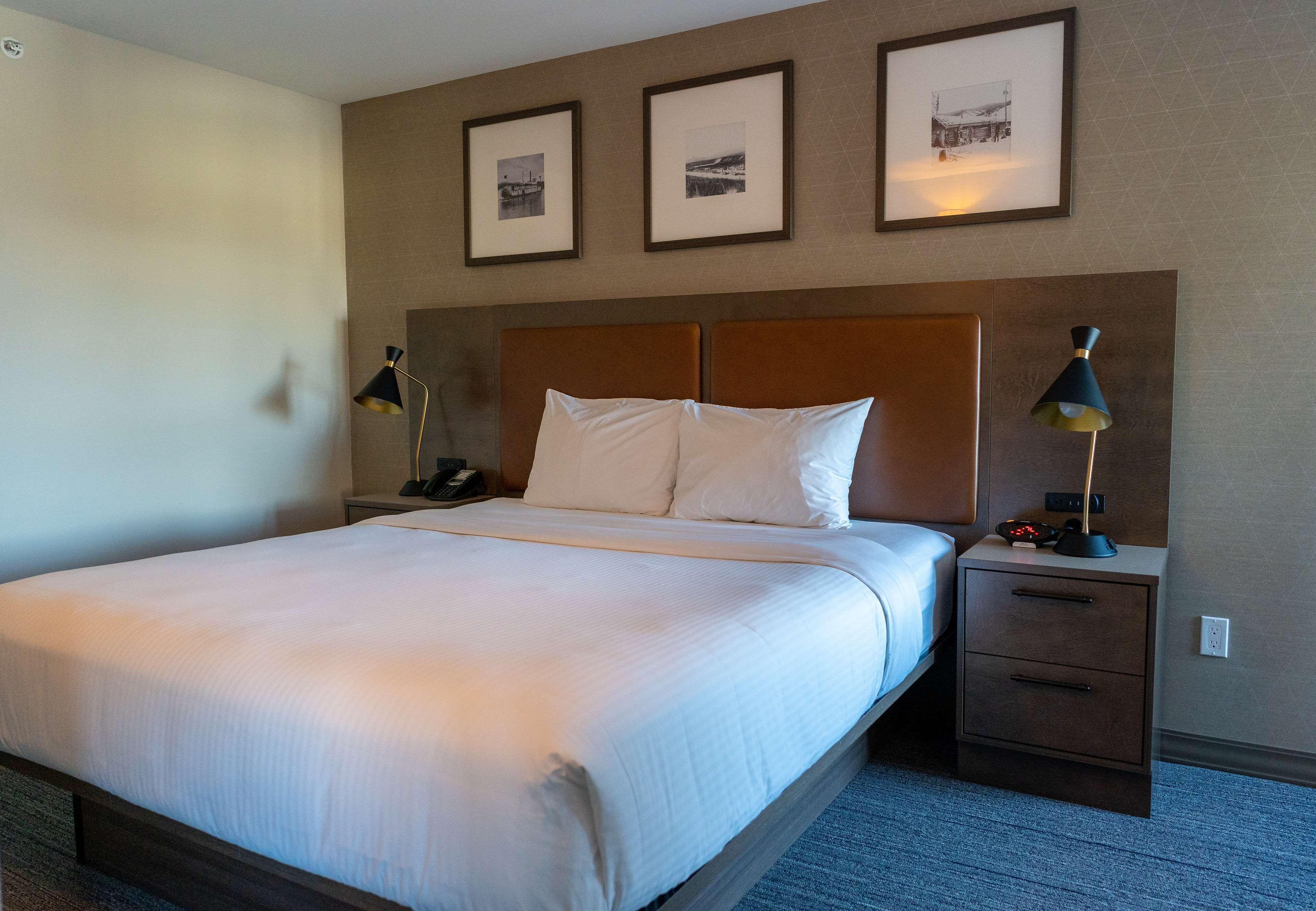 A hotel room with a large bed, two bedside tables, a nightstand, and three framed pictures on the wall.