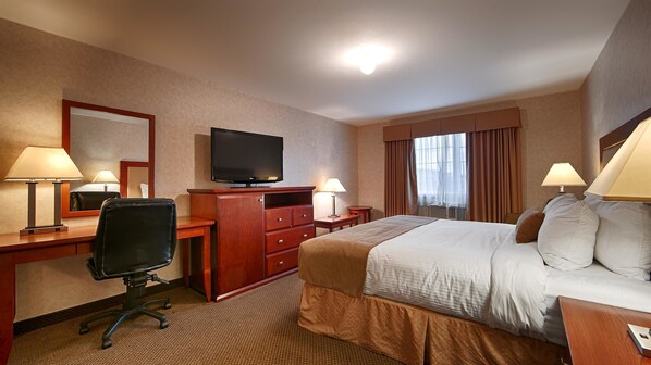 Quarto de hotel com cama, escrivaninha, cadeira, televisão e luminárias.