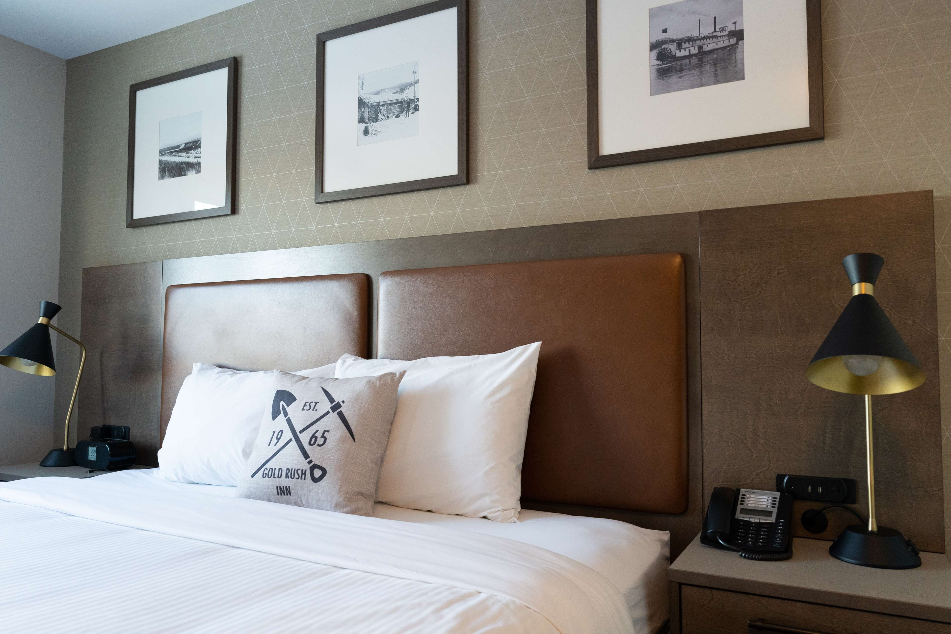 A hotel room with a large bed, two bedside lamps, a nightstand with a phone, and three framed pictures on the wall.