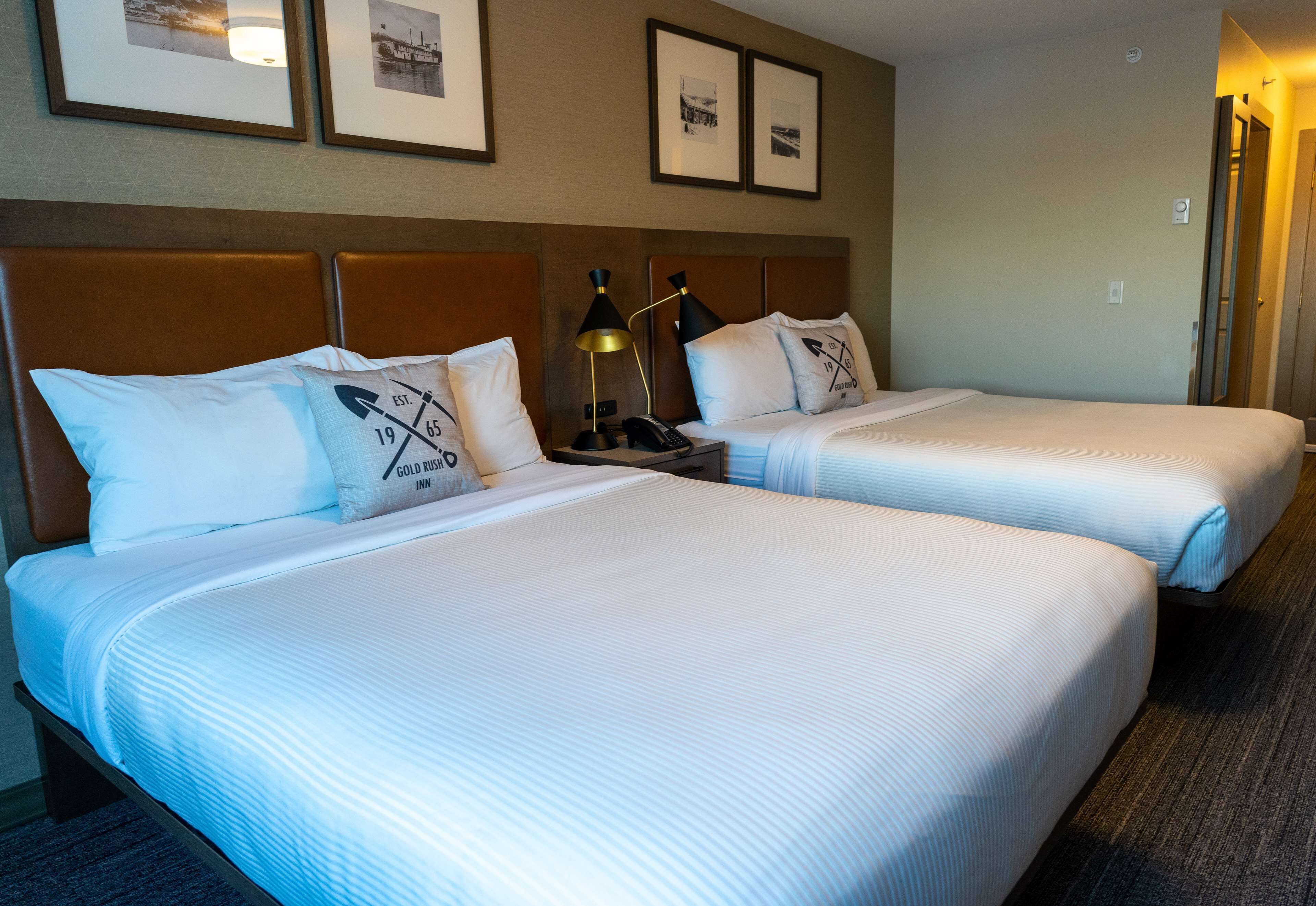 A hotel room with two beds, a nightstand with a lamp, and framed pictures on the wall.