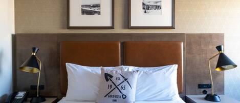 A neatly made bed with a pillow featuring a logo, two framed pictures on the wall, and bedside lamps on nightstands.