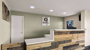 Una recepción con un cartel de 'Quality by Choice Hotels', una puerta blanca y un muro decorativo de madera.