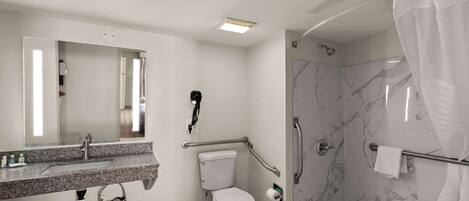 Un baño con pared de ducha de mármol, un inodoro blanco, un lavabo con espejo y un perchero para toallas.