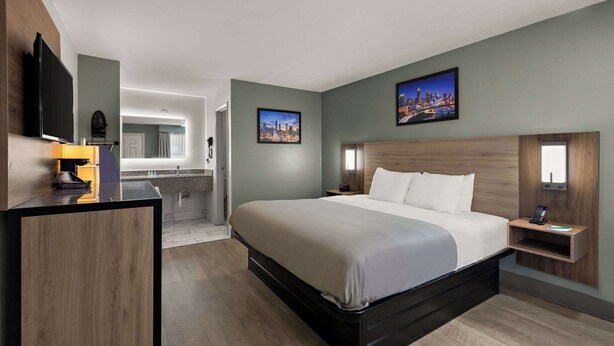Una habitación de hotel moderna con una cama grande, un escritorio, un televisor de pantalla plana y un baño visible al fondo.