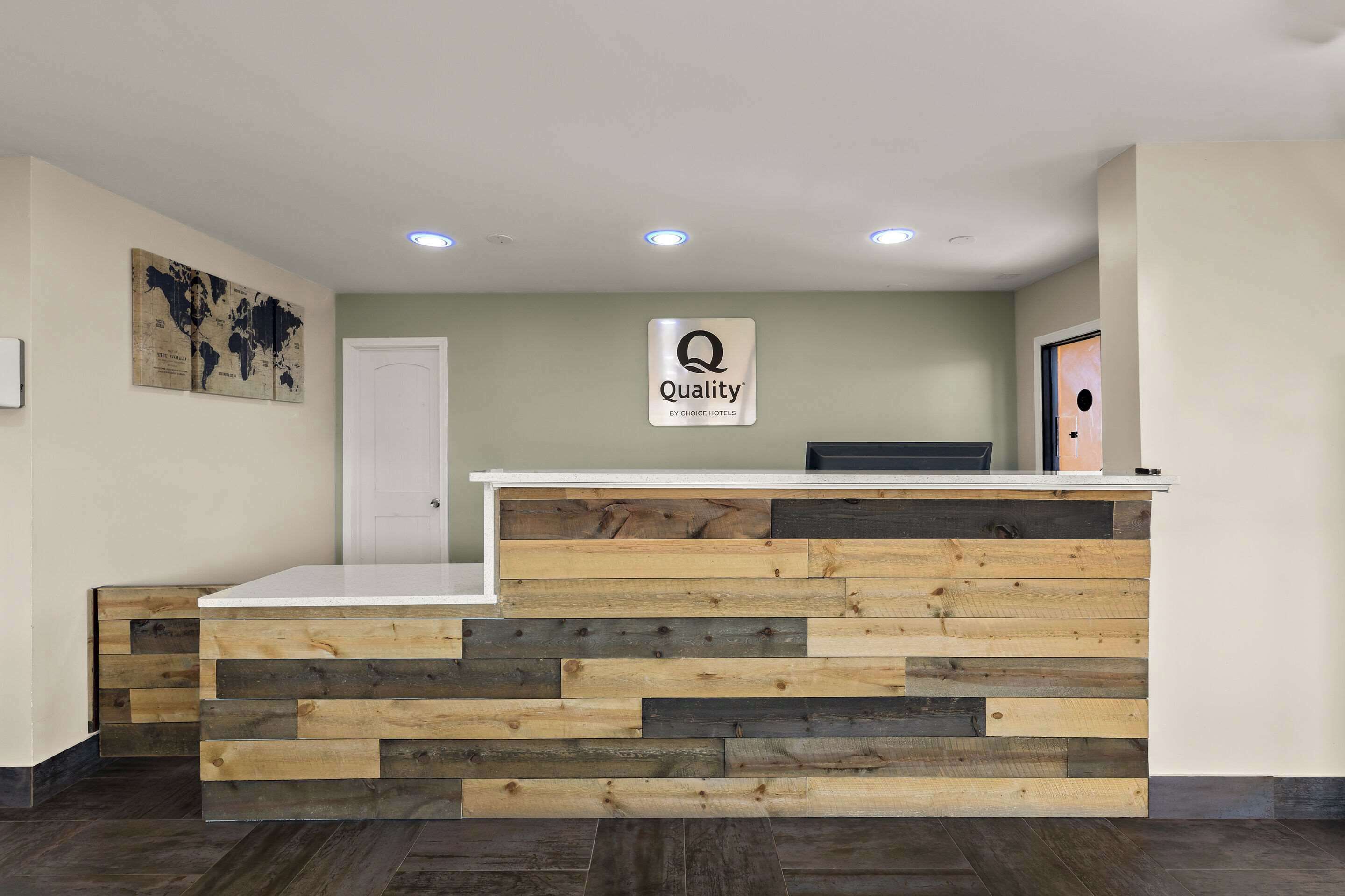 A reception desk with a 'Quality by Choice Hotels' sign, wooden paneling, and a world map on the wall.