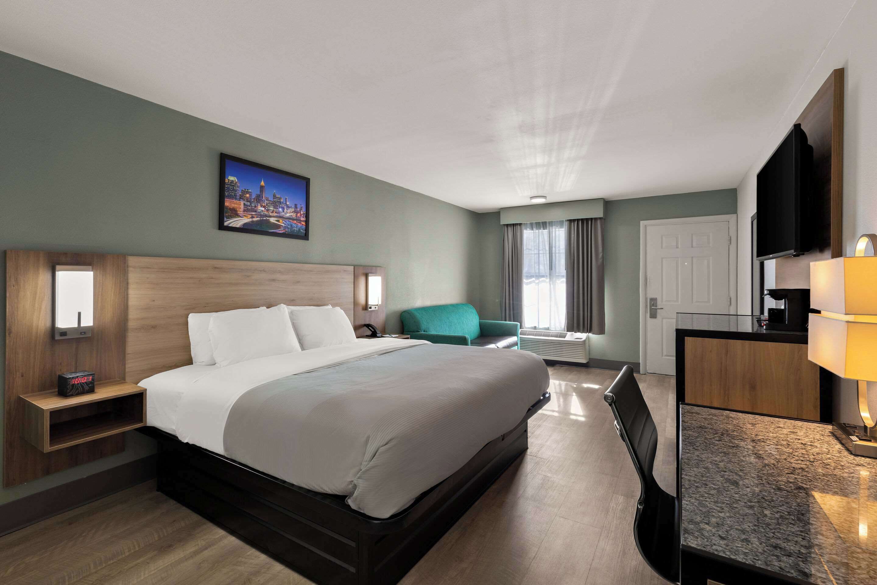 Une chambre d’hôtel avec un grand lit, un bureau avec une lampe, une télévision et un tableau représentant un paysage urbain accroché au mur.