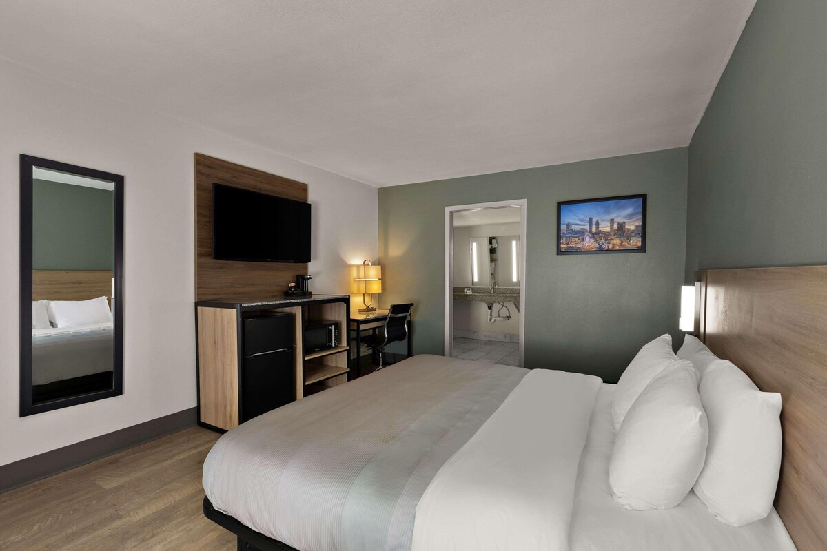 Habitación de hotel con cama, escritorio, televisor y baño visible a través de una puerta abierta.