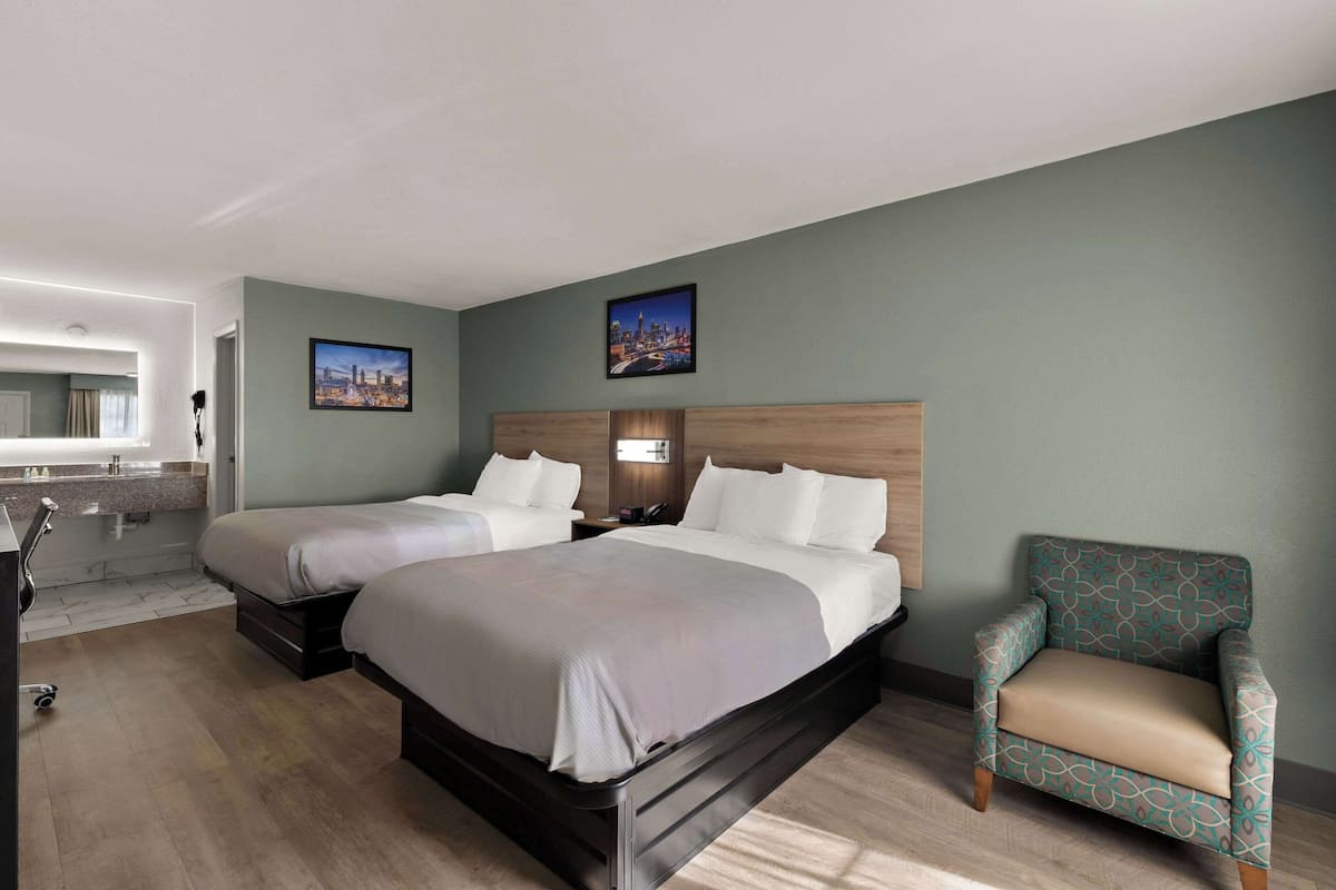 A hotel room with two beds, a chair, a desk, and a bathroom.